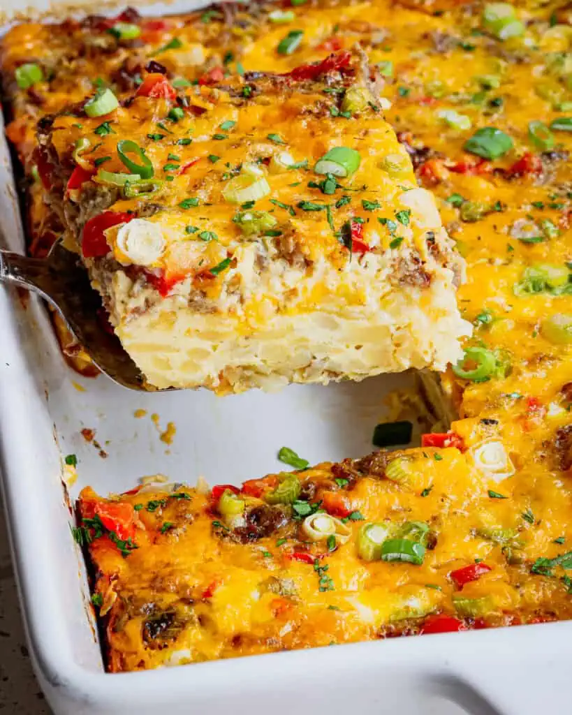 A piece of hashbrown breakfast casserole on a spatula over the rest of the cassserole dish. 