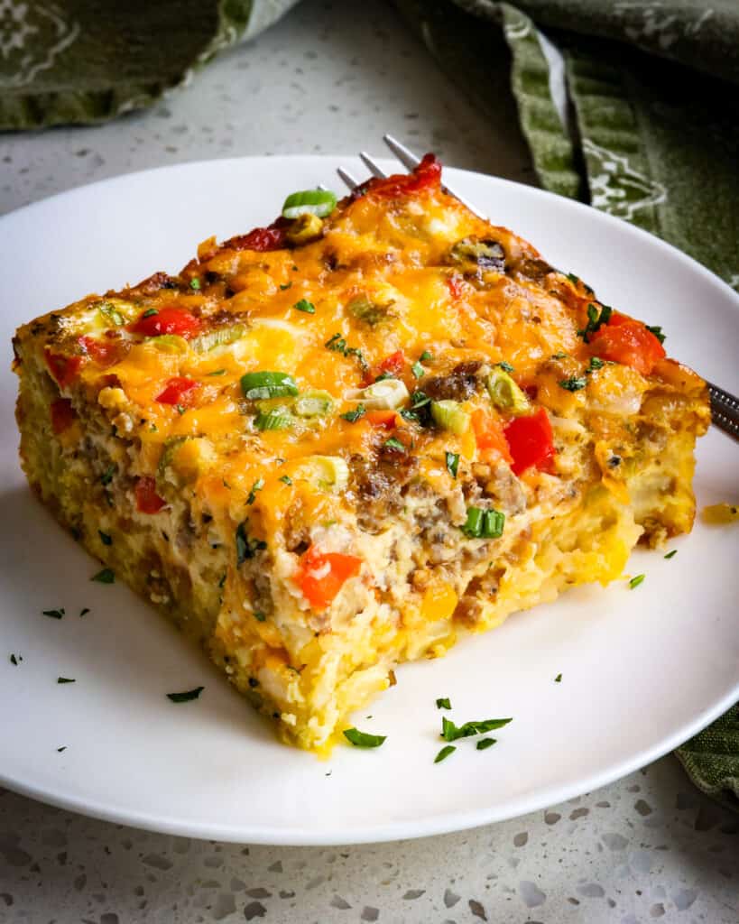 A piece of hashbrown breakfast casserole on a plate with a fork. 
