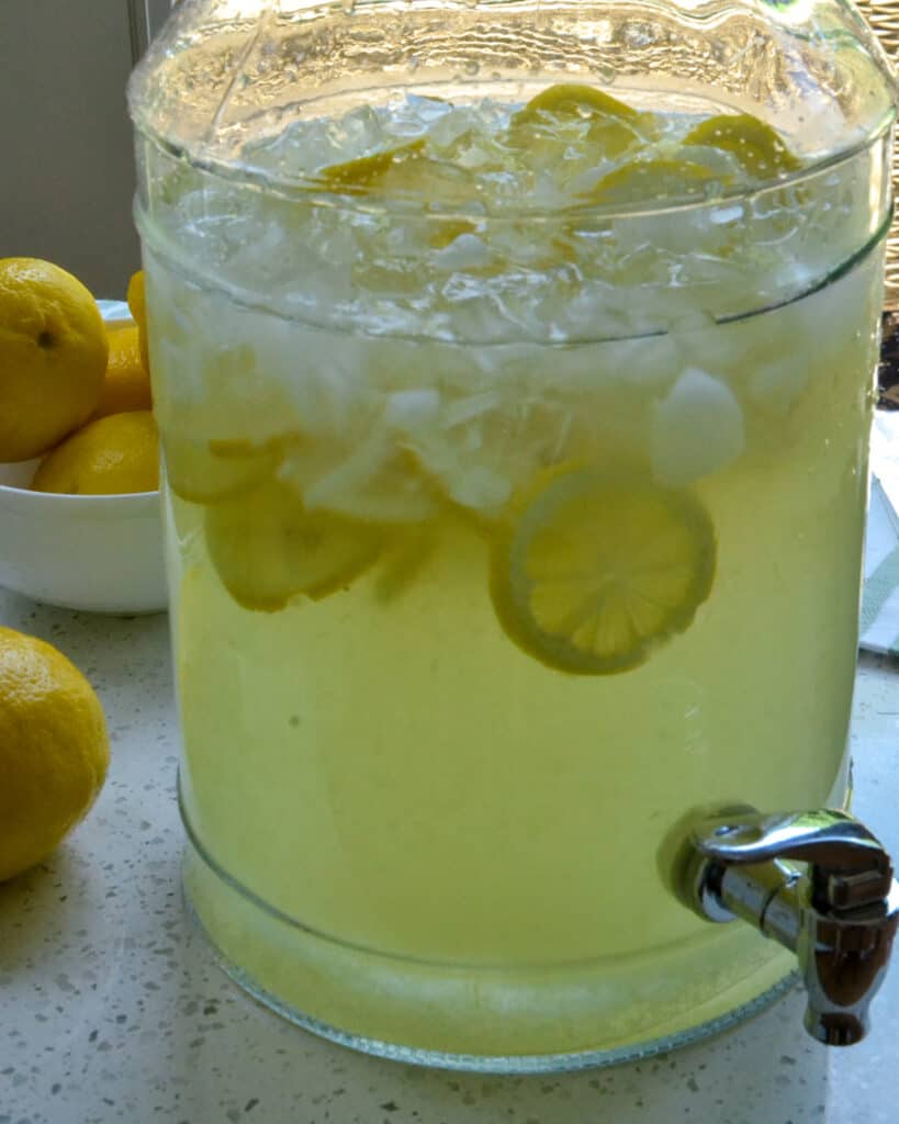A beverage decanter filled with fresh homemade lemonade, lemon slices, and ice. 