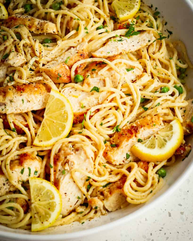 A large bowl full of spaghetti in a creamy lemon sauce and topped with sliced lemon pepper chicken.