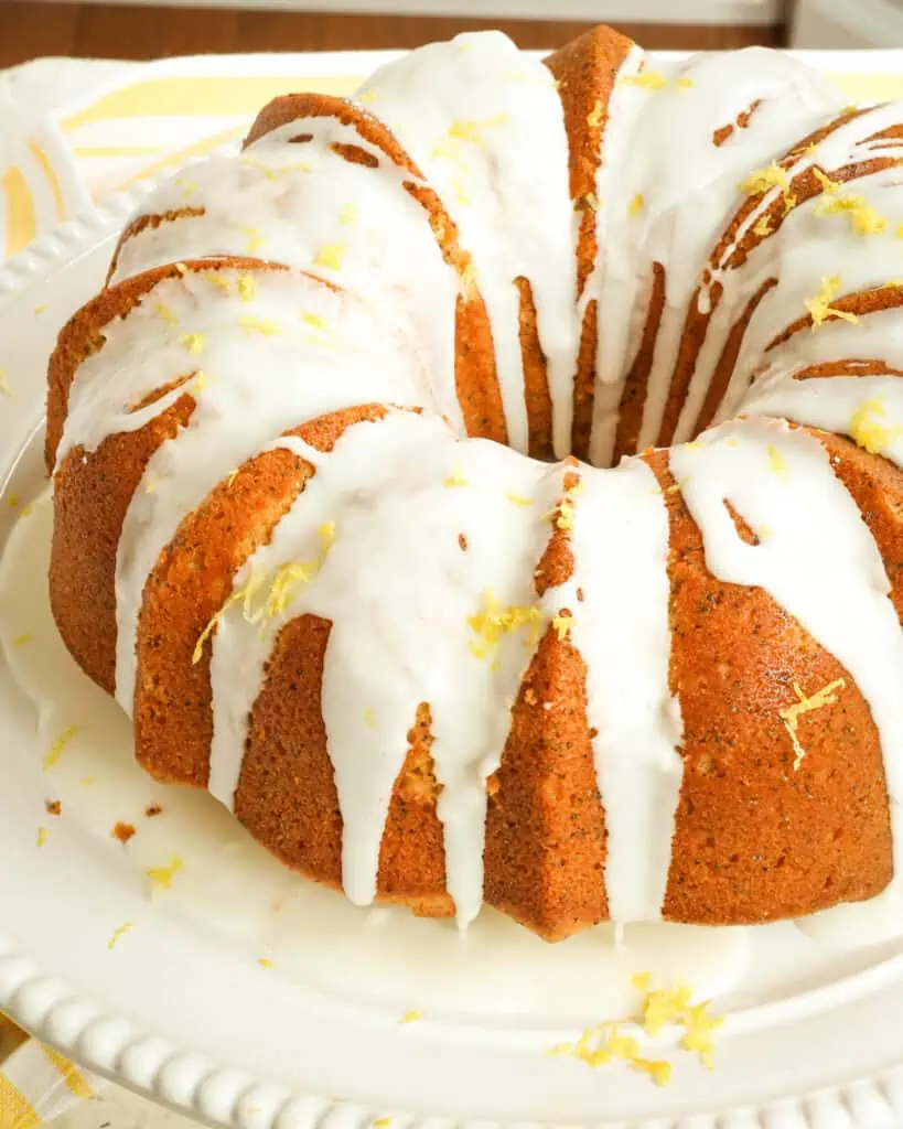 A made from scratch Lemon Poppy Seed Cake with a two ingredient lemon glaze on a white cake stand. 
