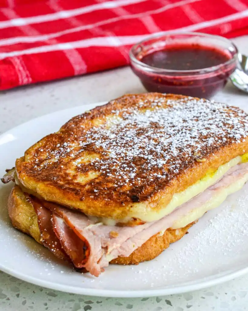 A whole monte cristo sandwich on a plate with a side of raspberry jam. 
