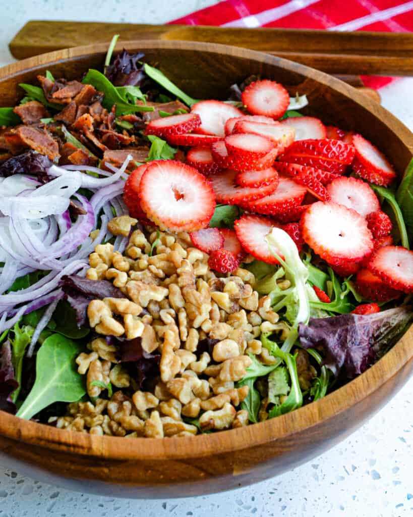 This delicious spring and summer salad combines fresh strawberries, crisp smoked bacon, sweet red onions, salty feta cheese, and crunchy walnuts with an easy-to-make six-ingredient creamy poppy seed dressing.