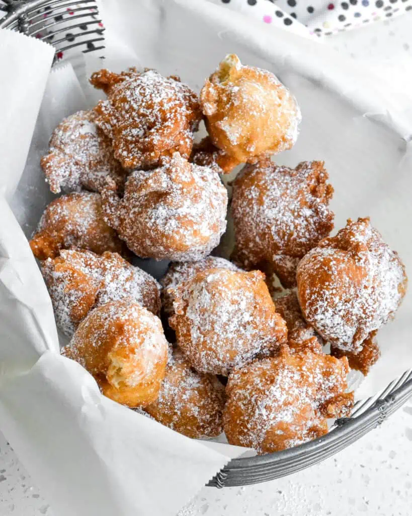Fried zeppoles coated with powdered sugar in a wire basket lined with parchment paper.
