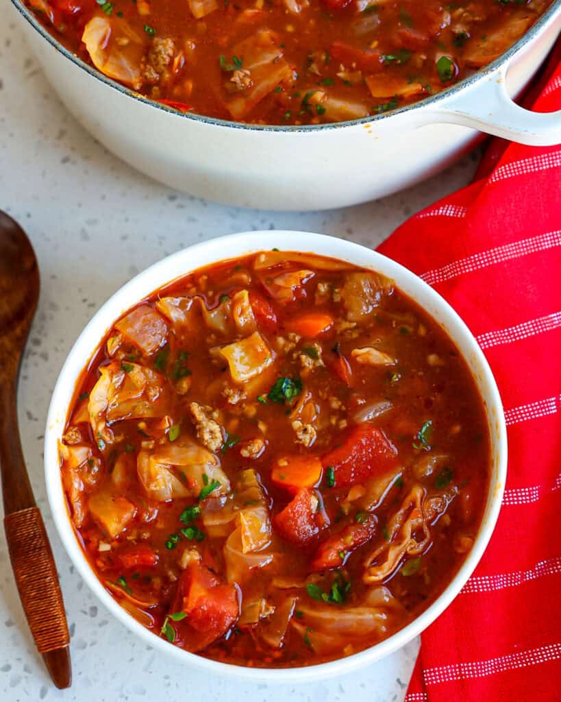 A single serving bowl of cabbage soup with a wooden spoon off to the side. 