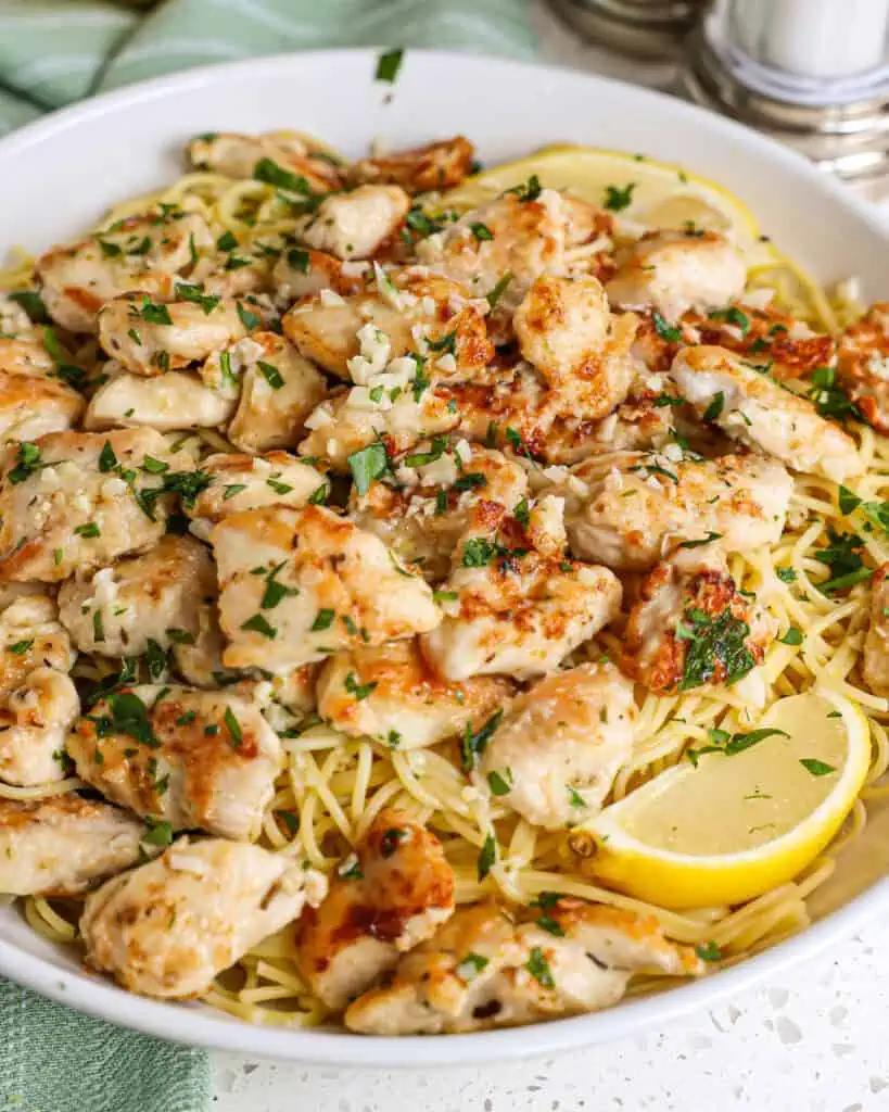 A scrumptious and easy Chicken Scampi recipe made with lightly breaded chicken bites, garlic, white wine, lemon juice, and parsley all on a bed of pasta topped with freshly grated Parmesan Cheese.