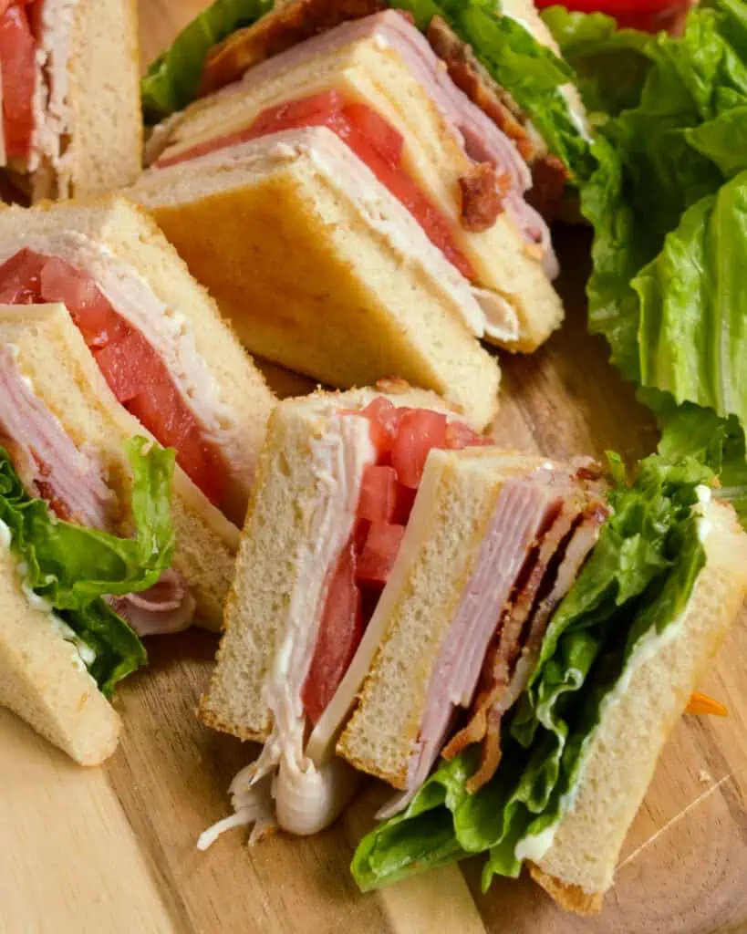 This classic New York club sandwich recipe is layered with smoky ham, roasted turkey, smoked bacon, crisp lettuce, juicy tomatoes, cheddar cheese, and mayonnaise spread on every slice of this triple-toasted bread extravaganza.
