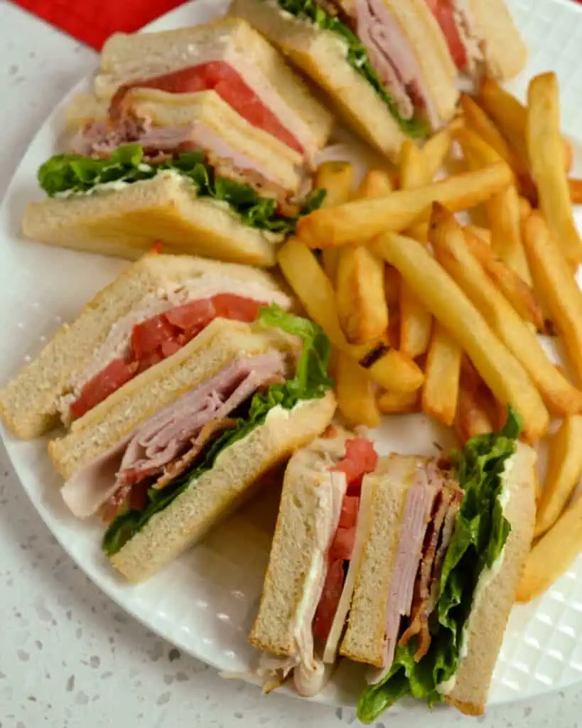 A classic mouthwatering good triple decker club sandwich with three slices of white bread toasted, mayonnaise, turkey, tomato, cheddar cheese, ham, crispy bacon, and lettuce.