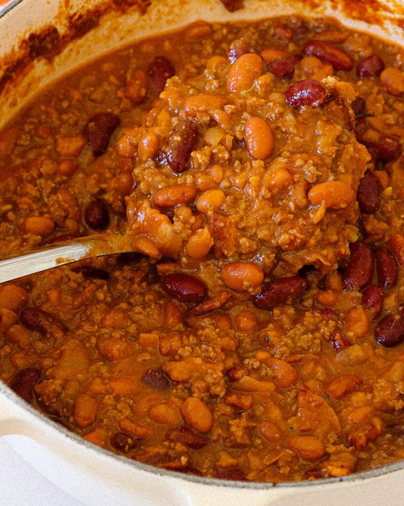 A ladle and a Dutch oven full of cowboy beans. 