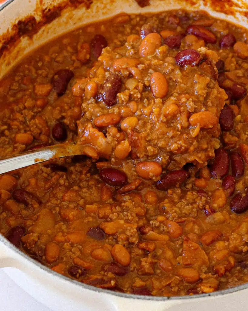 A Dutch oven and a ladle full of cowboy beans. 
