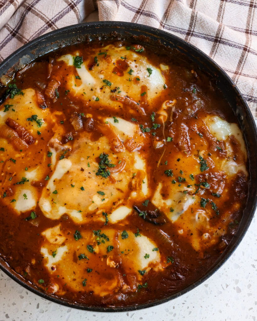 A skillet full of French Onion Chicken garnished with fresh herbs before serving.