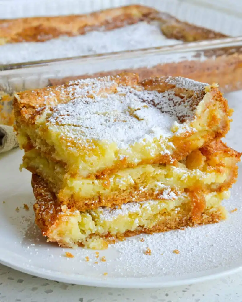 Three pieces of gooey butter cake stacked with the cake dish in the background. 