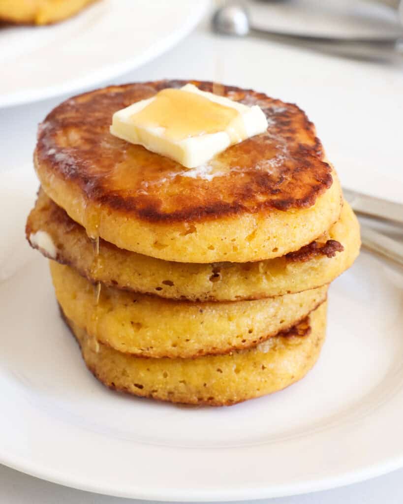Fried Johnny cakes with butter and maple syrup on a plate with a fork and a knife. 