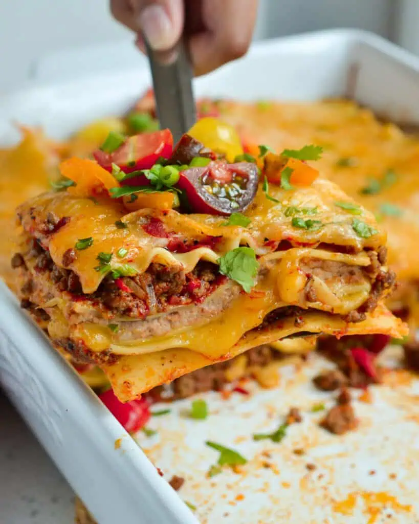 Mexican Lasagna is a hearty meal with an abundance of flavors from taco seasoned ground beef, onions, and refried beans. 