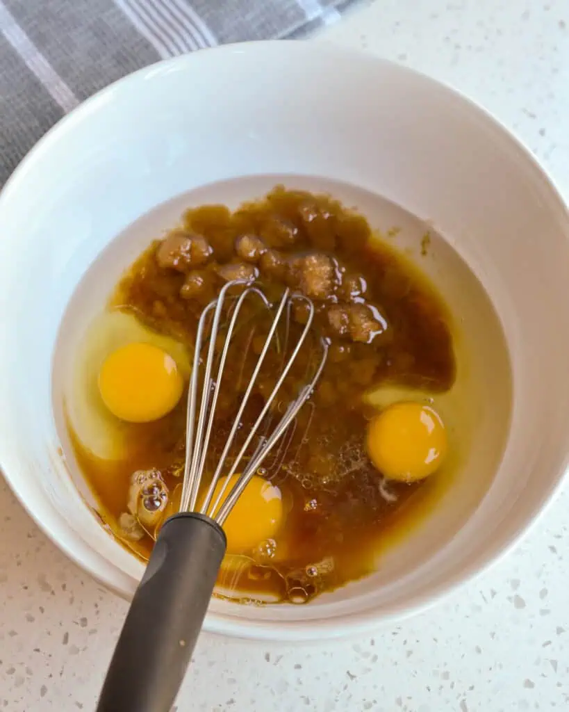 A medium bowl with eggs, oil, vanilla extract, brown sugar, carrots and apple. 