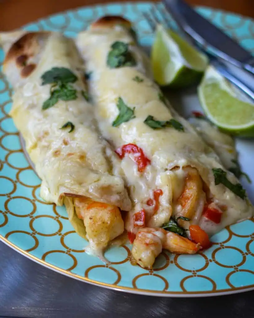 Two creamy shrimp enchiladas on a serving plate with limes. 