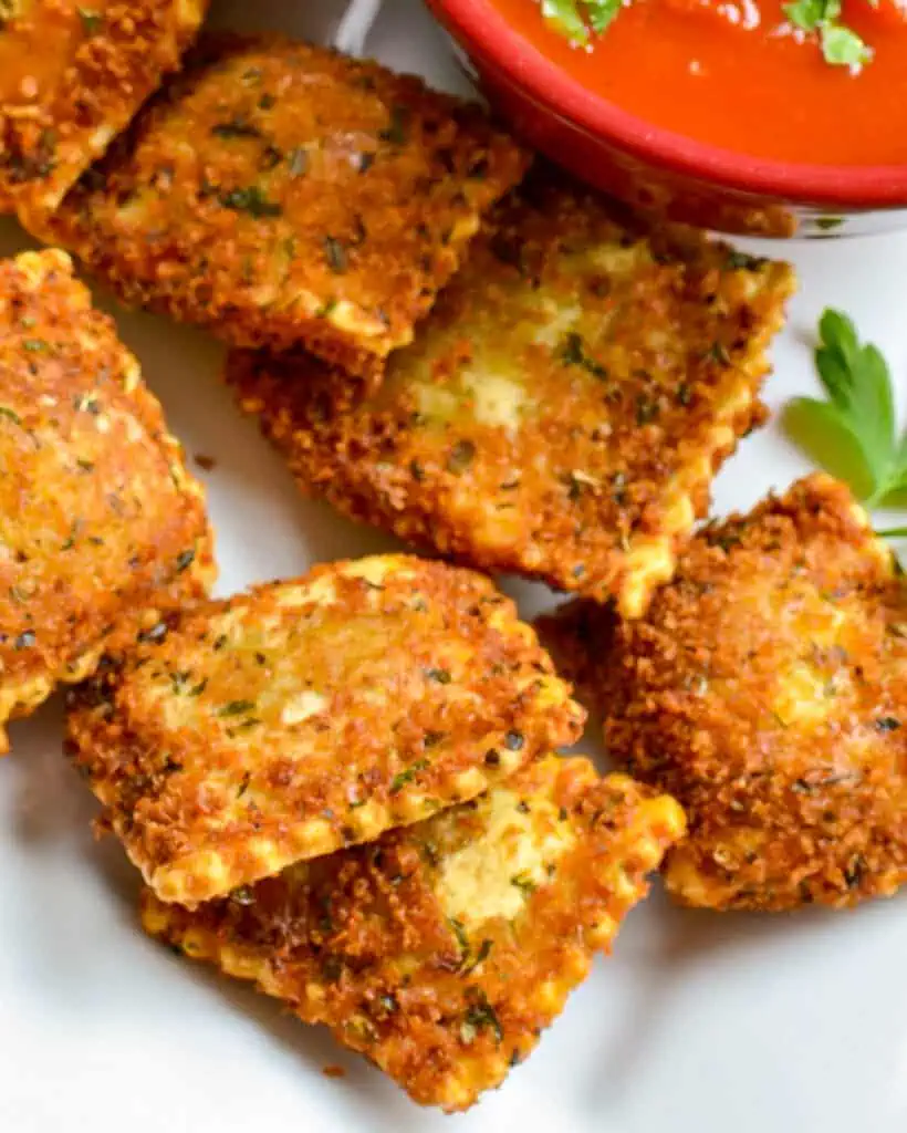A close up view of toasted ravioli on a white platter. 
