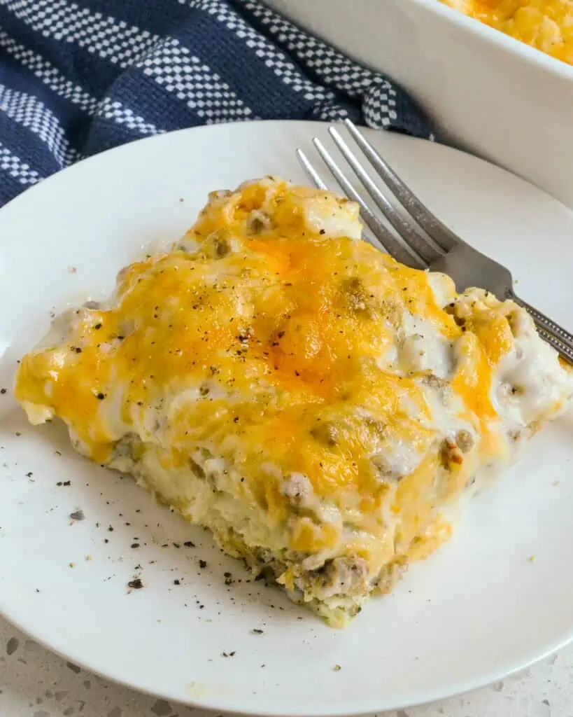 A slice of biscuits and gravy casserole on a serving plate with a fork. 