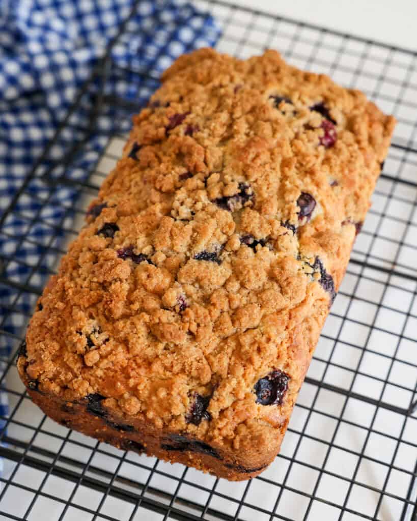 A loaf of blueberry bread cooling on a wire rack. 