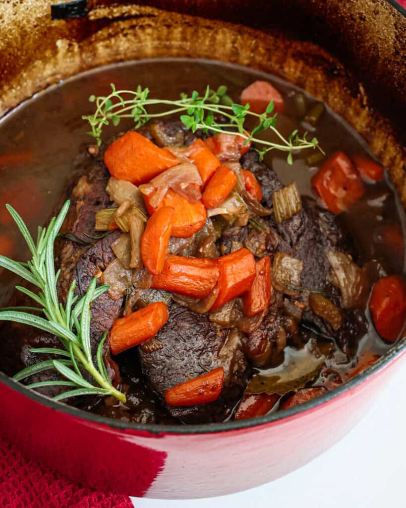 Tender slow cooked beef with onions, carrots. and fresh herbs in a Dutch oven. 