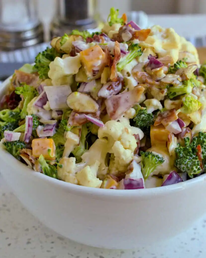 A bowl full of cream cauliflower and broccoli salad with almonds, onion, cheddar and bacon. 