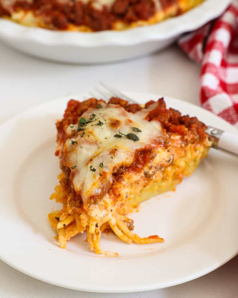 A piece of spaghetti pie on a plate with a fork. 