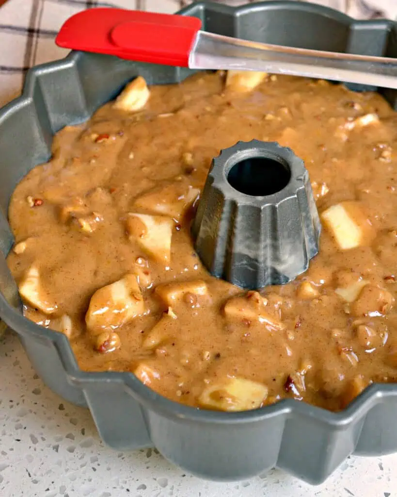 Apple cake batter in a bundt pan with a rubber spatula before being cooked. 