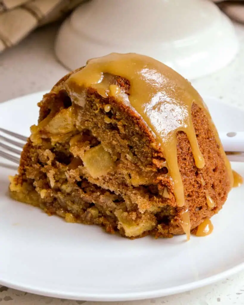 A piece of apple cake with caramel drizzle on a round plate. 