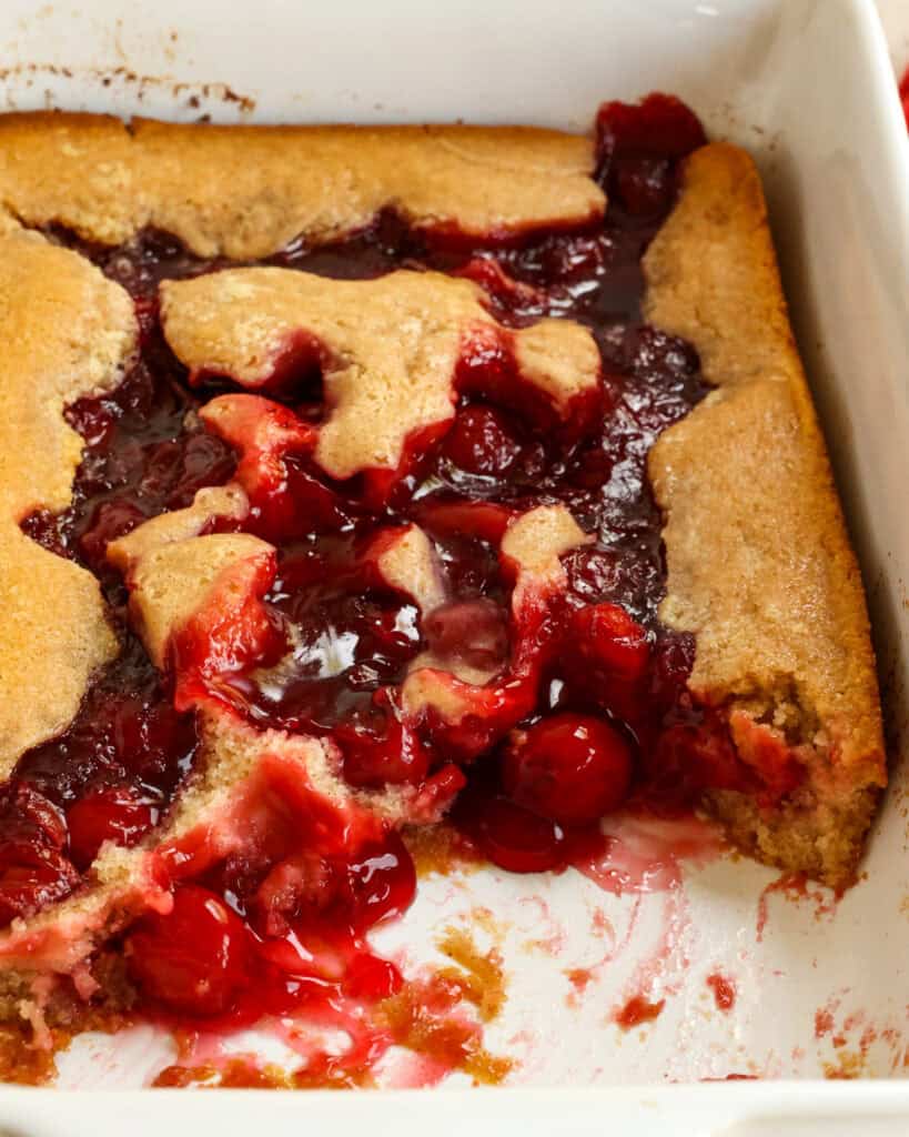 Cherry cobbler in a baking dish with a couple of scoops removed.