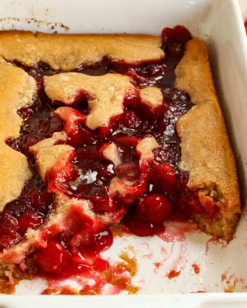 Cherry cobbler in a baking dish with a couple of scoops removed. 