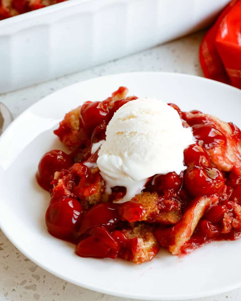 Cherry cobbler with a scoop of melting vanilla ice cream on a single serving plate.