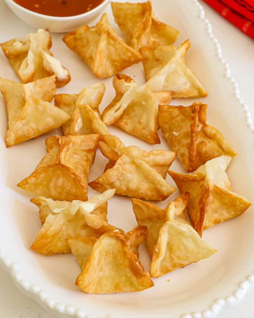 Cream cheese filled wontons on a serving platter with sweet and sour sauce.