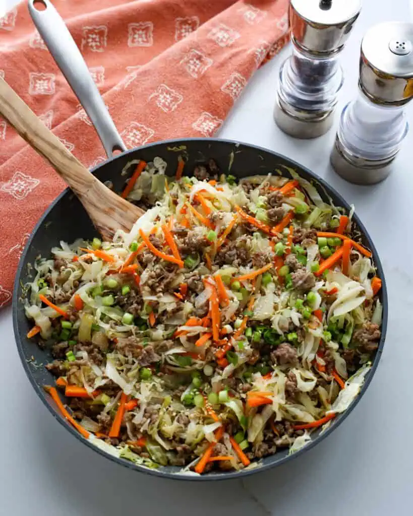 An ovehead view of skillet full of egg roll in a bowl with an orange kitchen towel in the background.