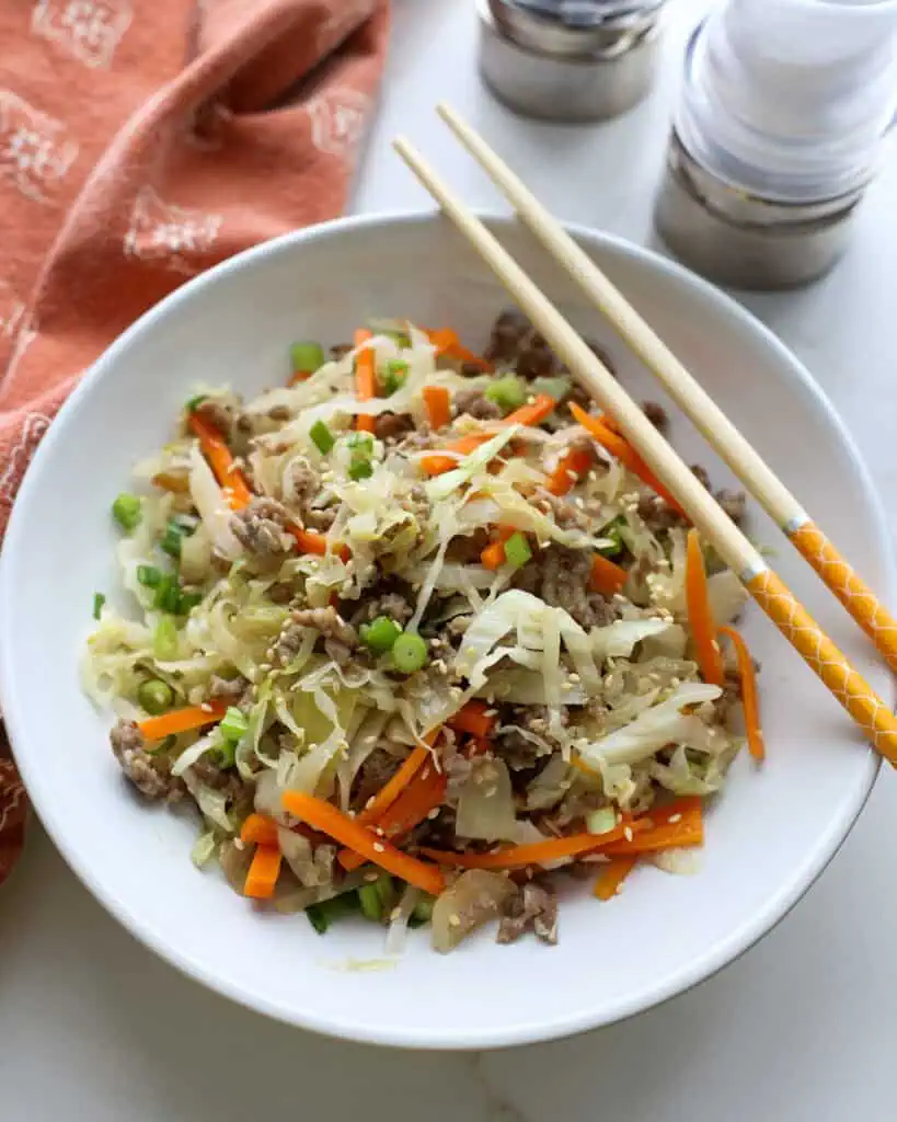A single serving bowl full of egg roll in a bowl with chopsticks and a salt and pepper shaker in the background.
