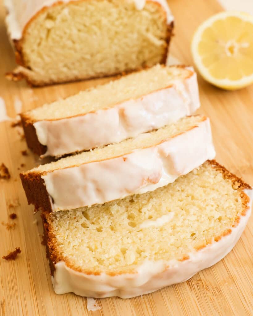 Sliced lemon loaf on a cutting board with fresh lemons. 
