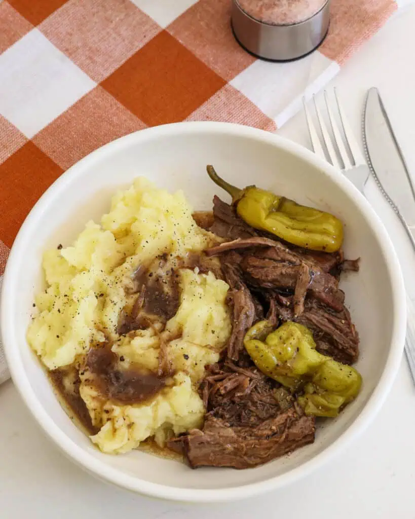 A bowl full of Mississippi por roast, mashed potatoes, and gravy.