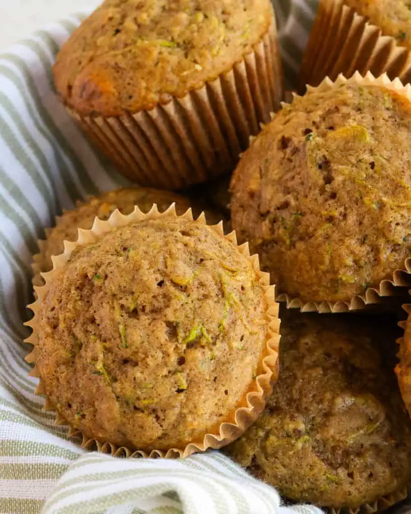 A basket full of zucchini muffins with fresh zucchini and chopped pecans.