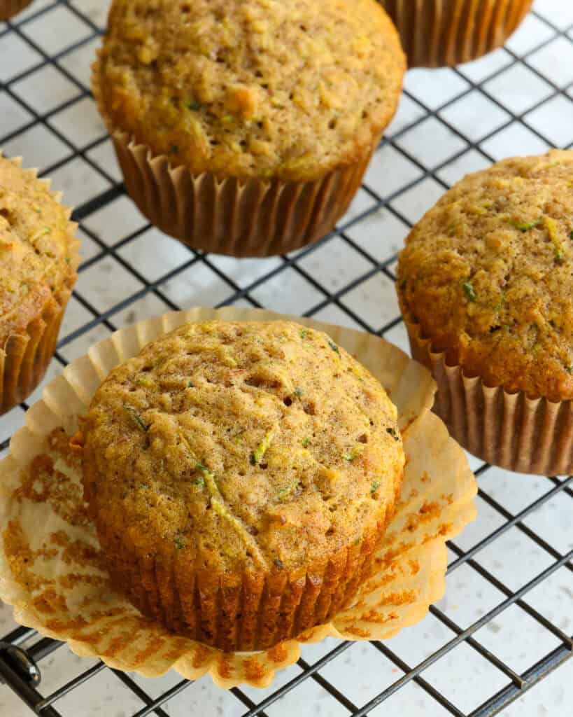 A zucchini muffin with the baking cup removed on a cooling rack. 