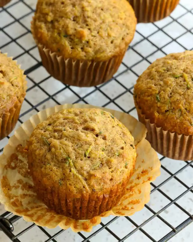A zucchini muffin with the baking cup removed on a cooling rack.