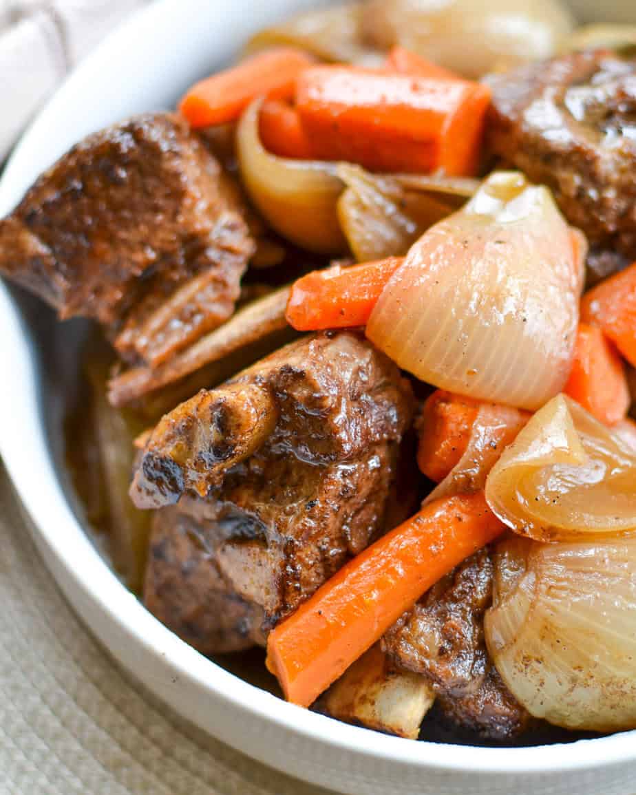 Slow cooked short ribs, onions, and carrots in a white serving bowl.