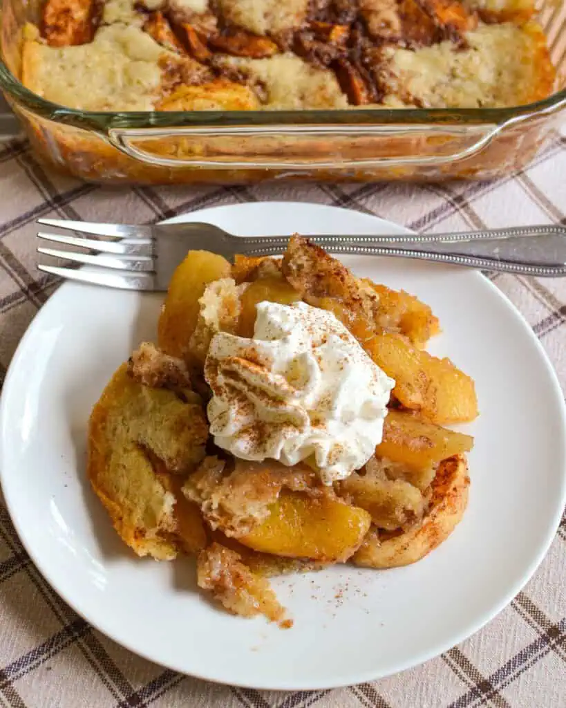 Apple cobbler topped with whipped cream and cinnamon on a single serving plate. 