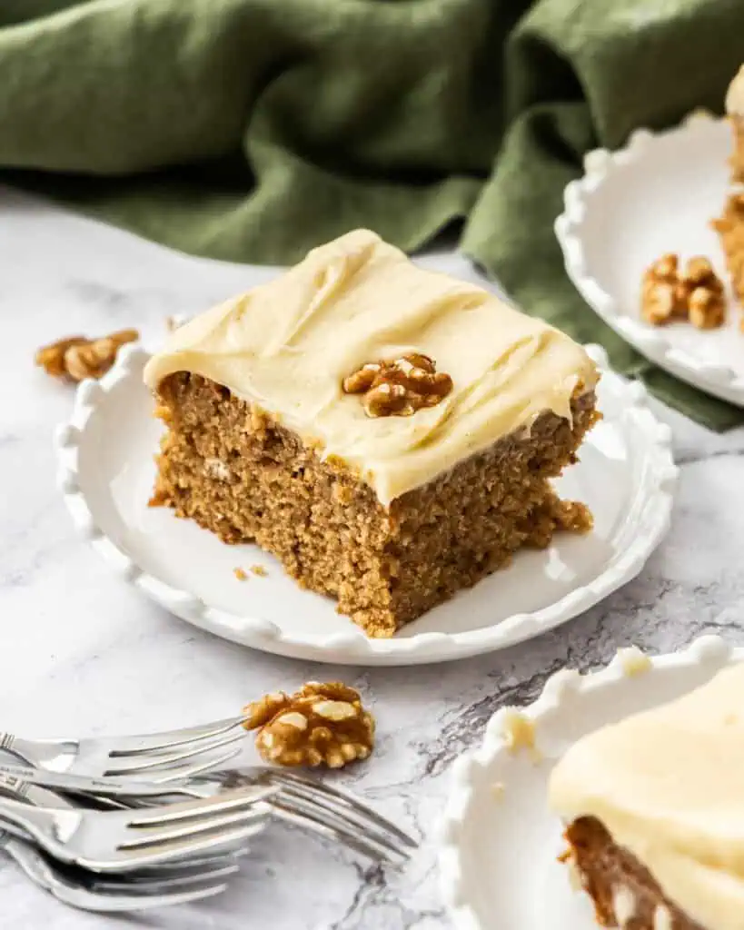 Pieces of applesauce cake on dessert plates with forks in the foreground and  a green towel in the background. 