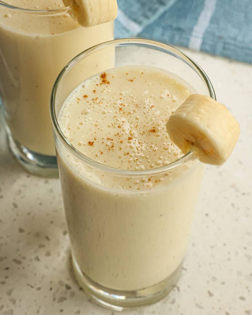 Two banana smoothies with a sprinkle of cinnamon and a slice of banana. 