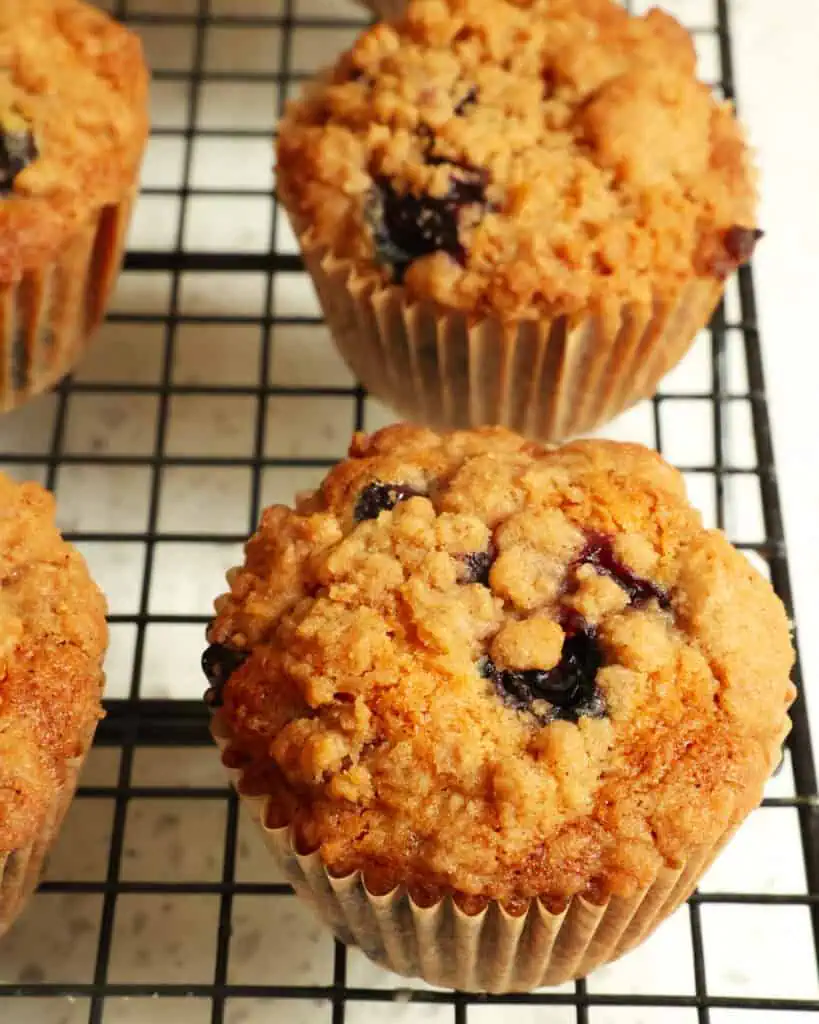 Multiple blueberry muffins on a wire rack cooling. 