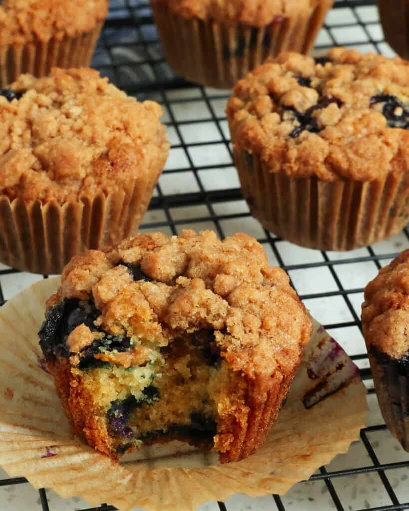 Multiple bueberry muffins on a wire cooling rack. One has been bitten into. 