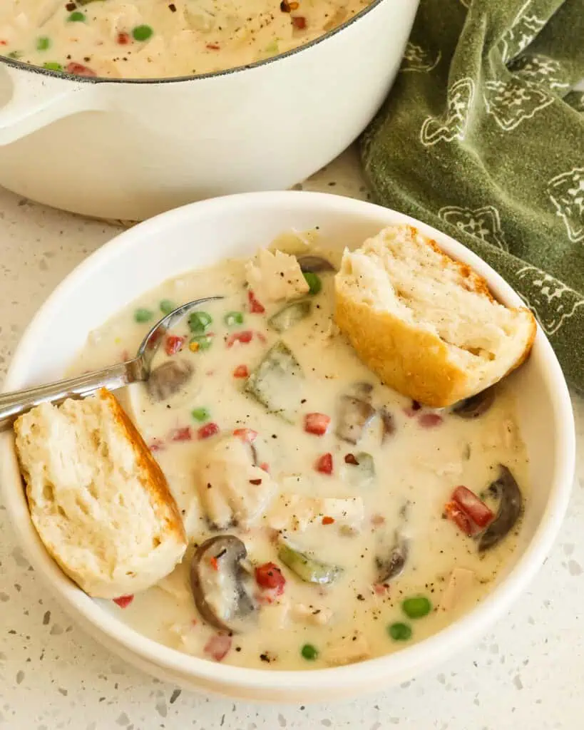 A single serving bowl full of chicken a la king with a biscuit. 