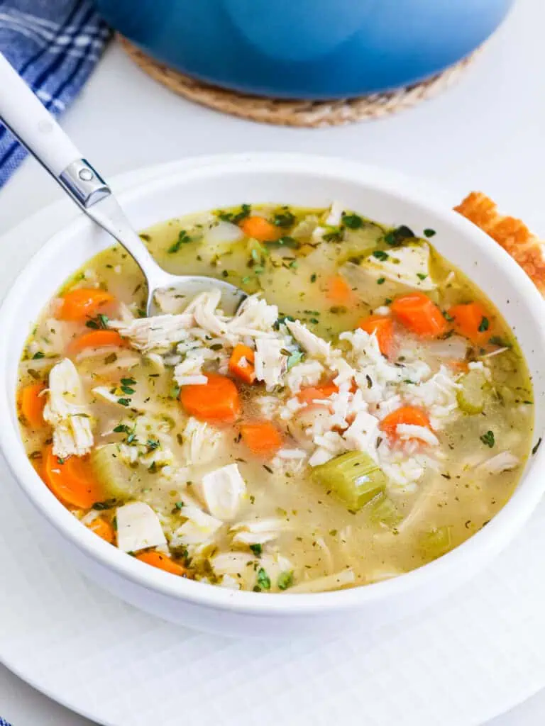 An individual bowl of chicken rice soup with a crusty French bread. 