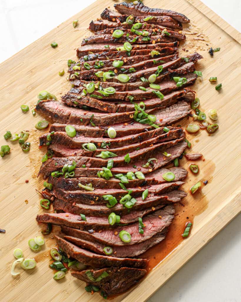 Thinly sliced flank steak on a wooden cutting board. 