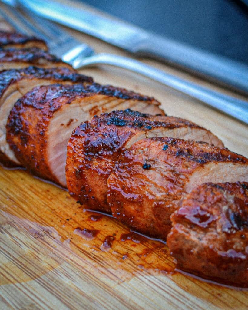 How to Grill Pork Tenderloin Grilled Pork Tenderloin sliced on a cutting board with a fork and knife behind.