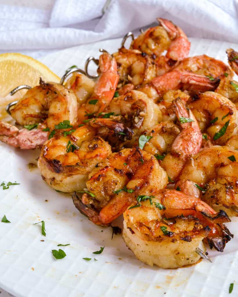 Grilled shrimp on skewers with fresh herbs and lemon wedges.